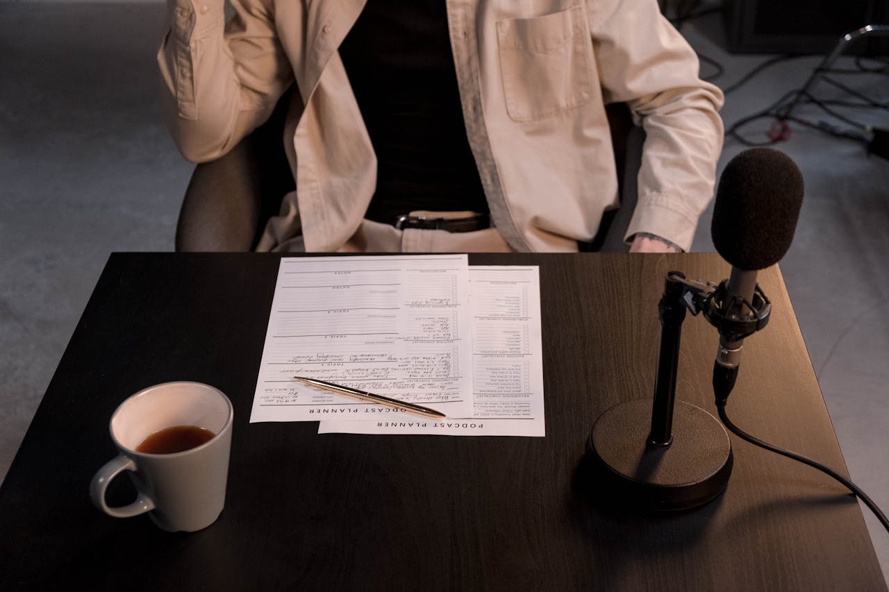 A podcast setup with microphone, papers, and coffee cup on a desk.