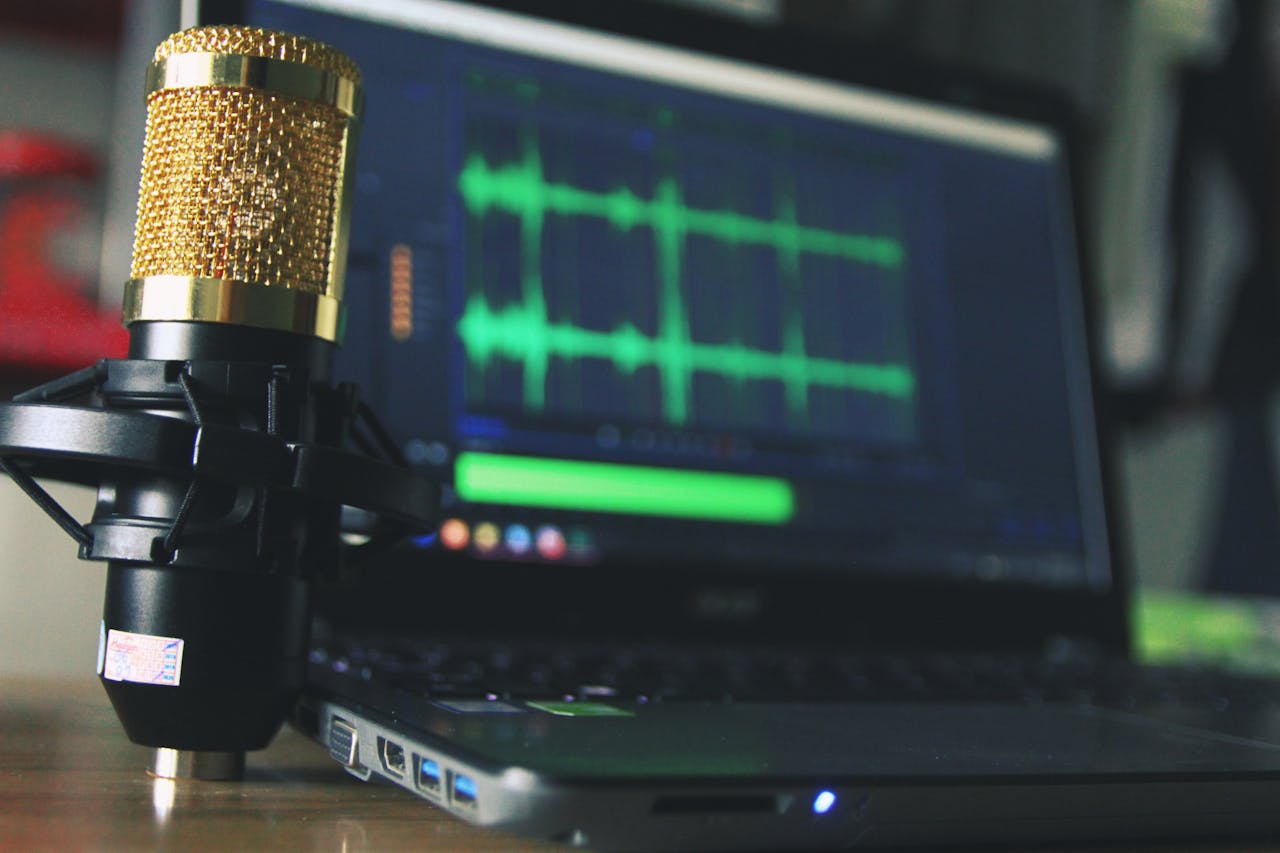 Close-up of a golden microphone and laptop used for audio editing.